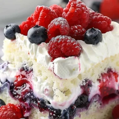 Delicious Summer Berry Poke Cake topped with vibrant mixed berries.