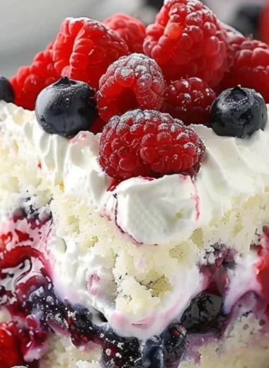 Delicious Summer Berry Poke Cake topped with vibrant mixed berries.