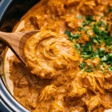 Delicious crockpot butter chicken served with rice and garnished with cilantro.