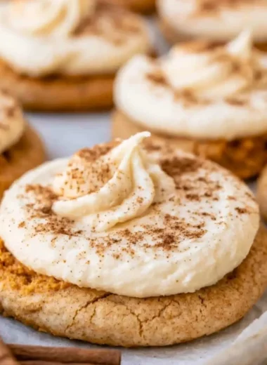 Pumpkin cookies with cream cheese frosting displayed on a rustic wooden table.