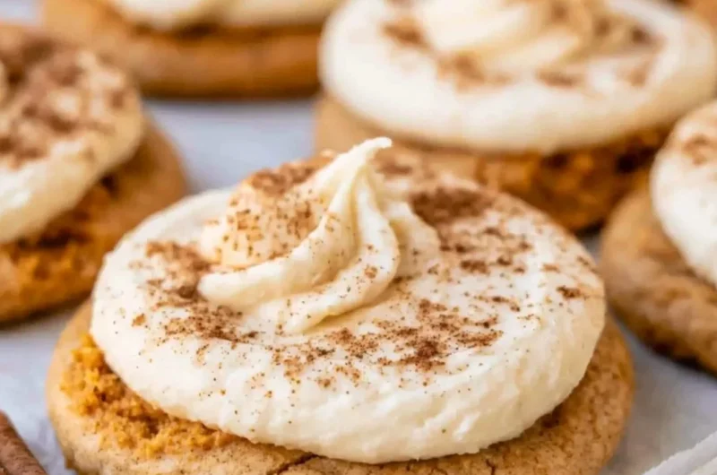 Pumpkin cookies with cream cheese frosting displayed on a rustic wooden table.