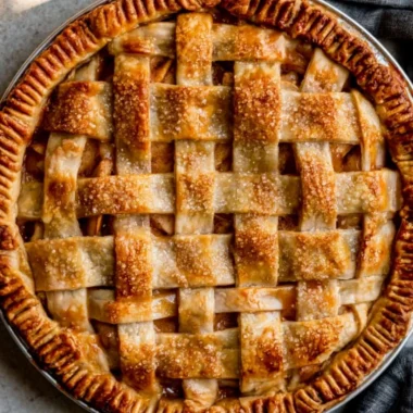 Slice of caramel apple pie topped with caramel drizzle and fresh apple slices.