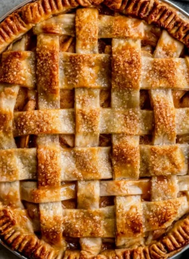 Slice of caramel apple pie topped with caramel drizzle and fresh apple slices.