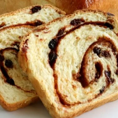 Loaf of homemade cinnamon swirl raisin bread on a wooden cutting board
