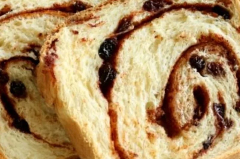 Loaf of homemade cinnamon swirl raisin bread on a wooden cutting board